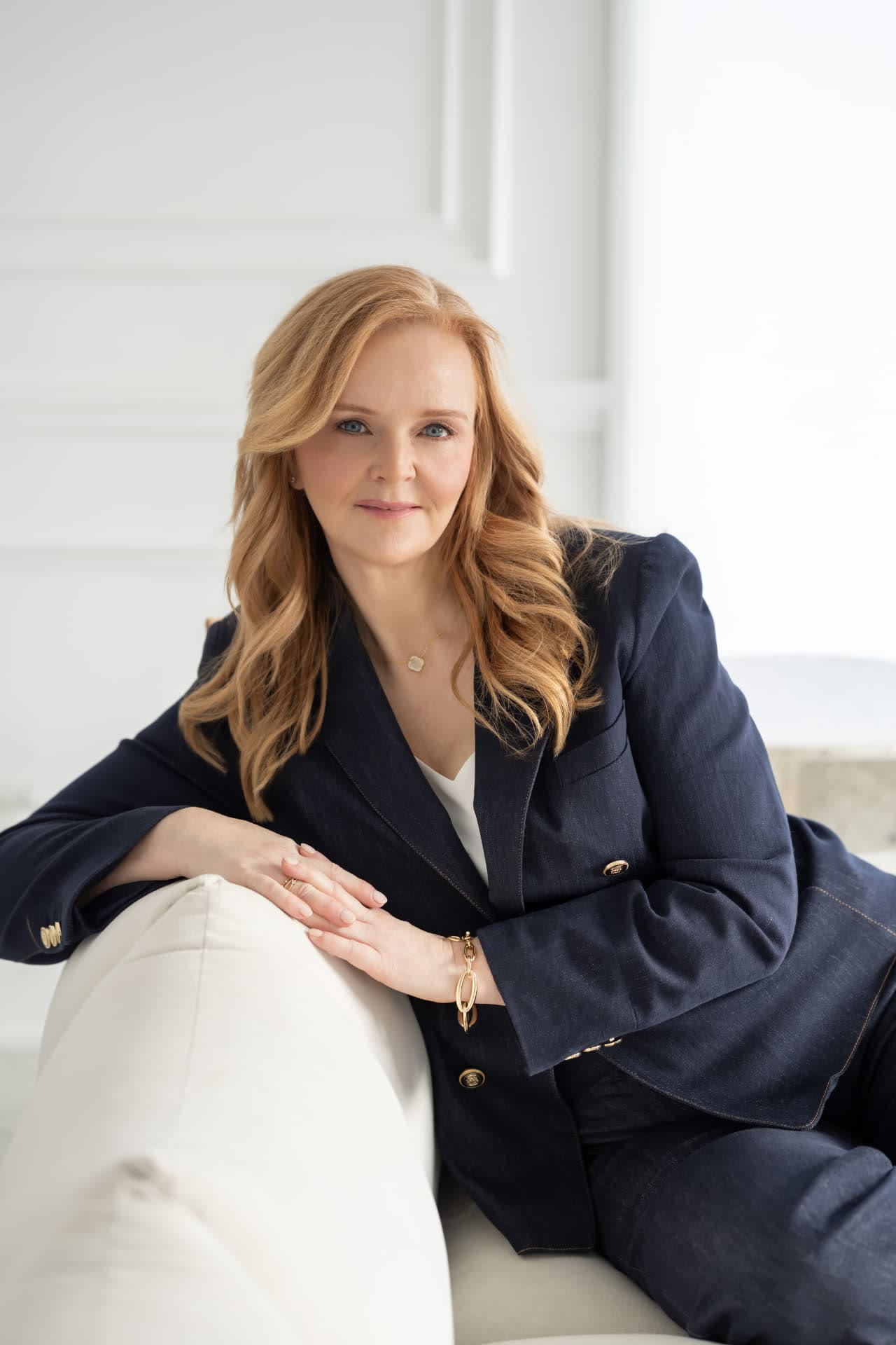 Camille Glover seated and leaning forward, wearing a navy jacket with gold buttons over a white top